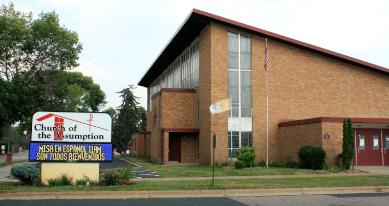 Photo of the entrance to the Church of the Assumption, including its sight which has the name in English but a scrolling text sign in Spanish.