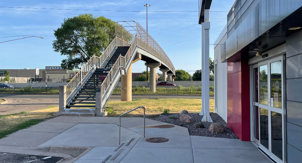 Modern full-color view from the ground looking at approximately the same angle from the front door of Grainger toward the bridge.  Menards is in the background.